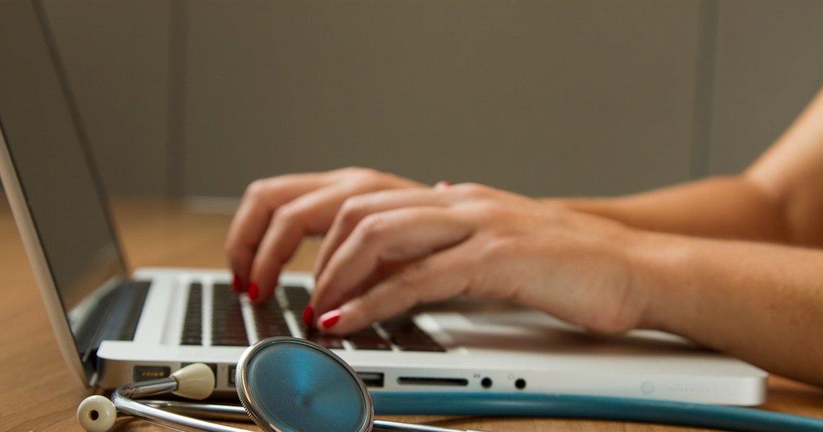 Doctor typing on a laptop with a stethoscope on the desk